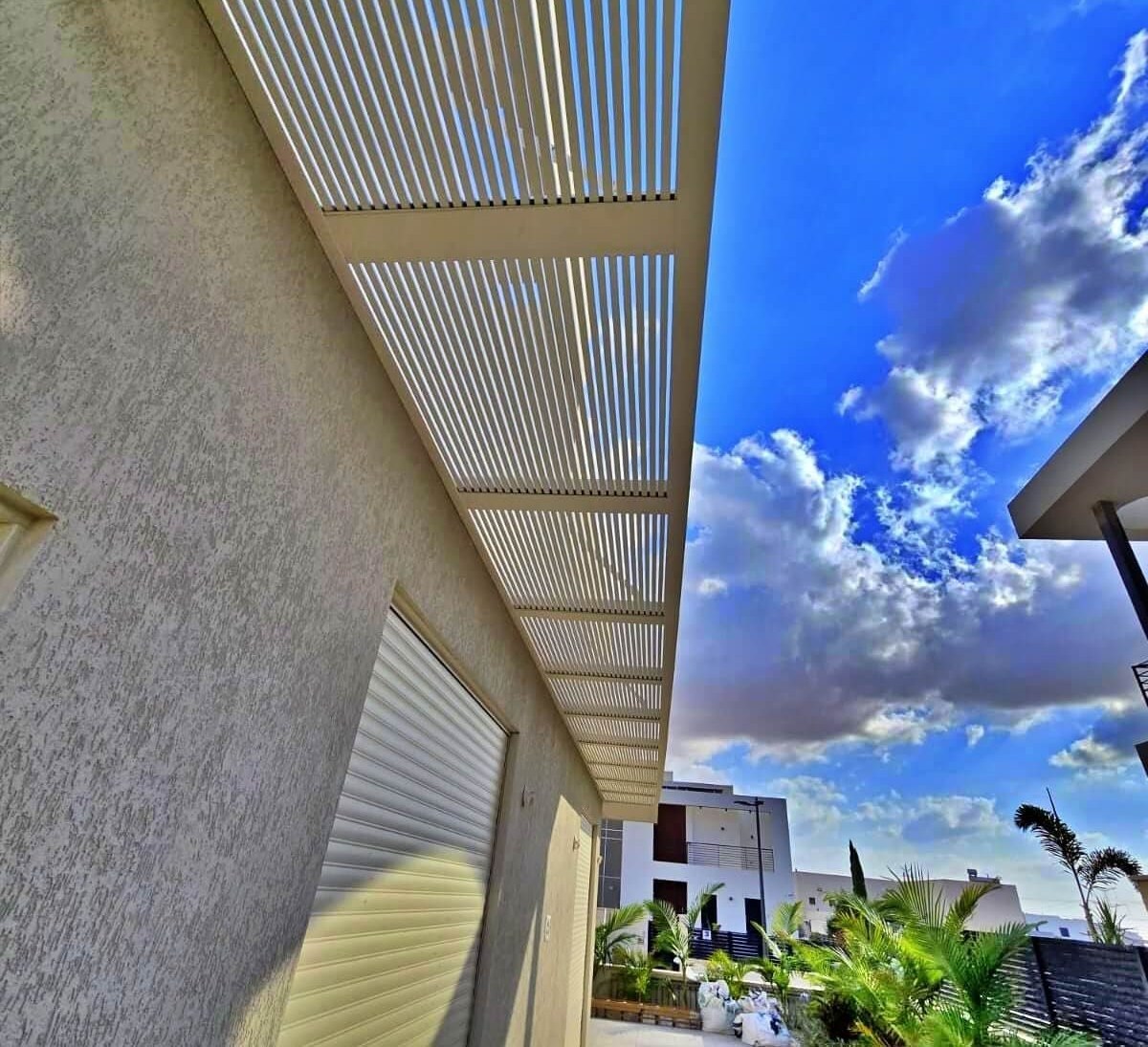 פרגולת אלומיניום לאורך קיר הבית, מתחת לשמיים כחולים
